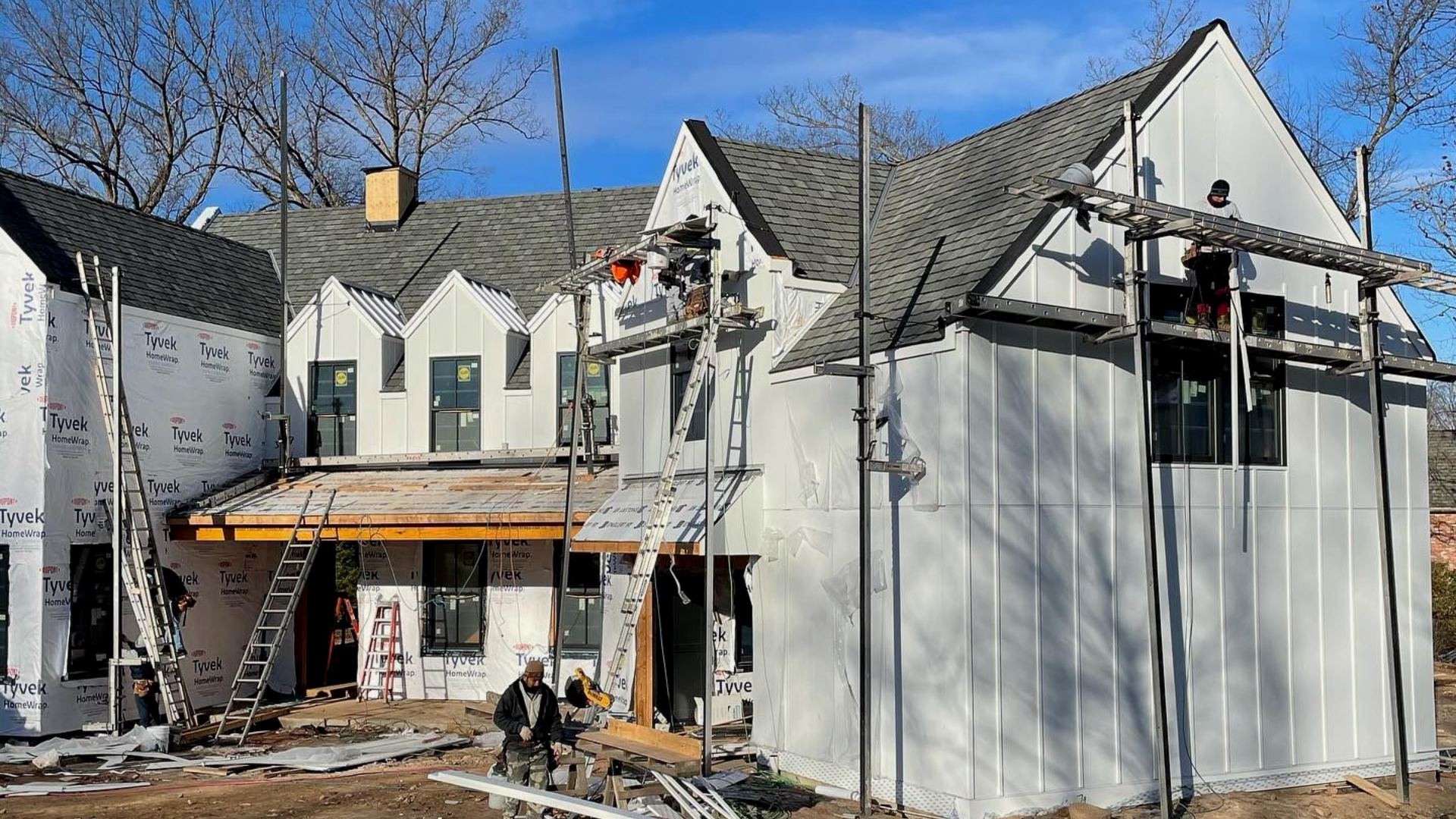 White house under renovation with scaffolding, exposed siding, flashing, and a porch roof in front being installed by the Paese team