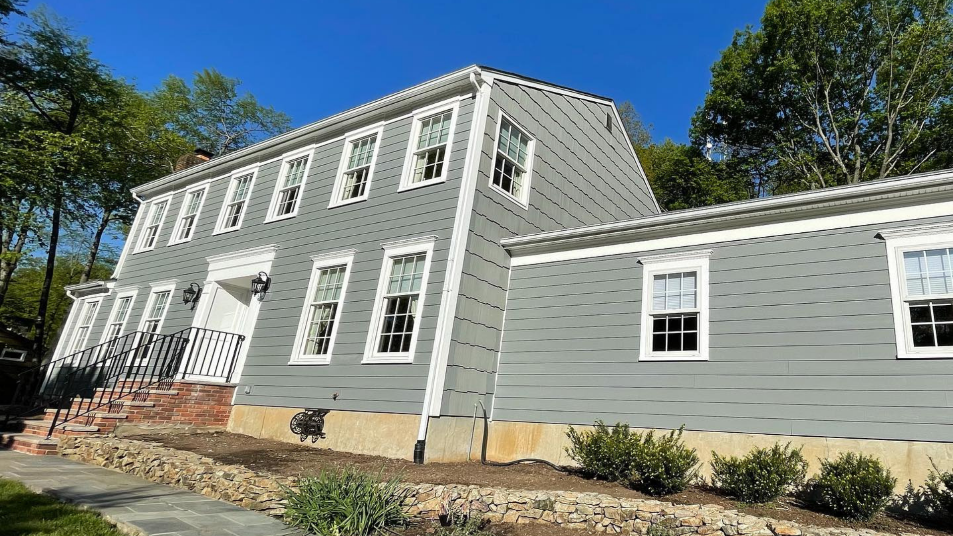 Gray two-story house with white trim and attached single-story wing, viewed from the front on a sunny day (a project of Paese Construction LLC)