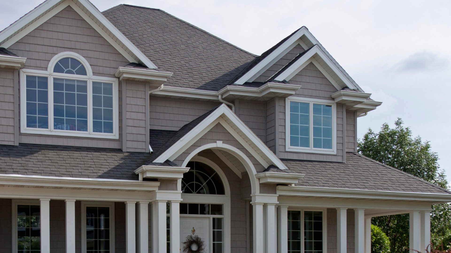 Large gray two-story suburban house with white trim, arched entryway, and front porch