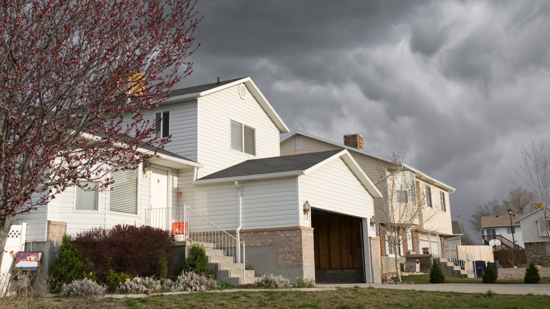 Suburban house with garage and leafless trees under a dark, stormy sky