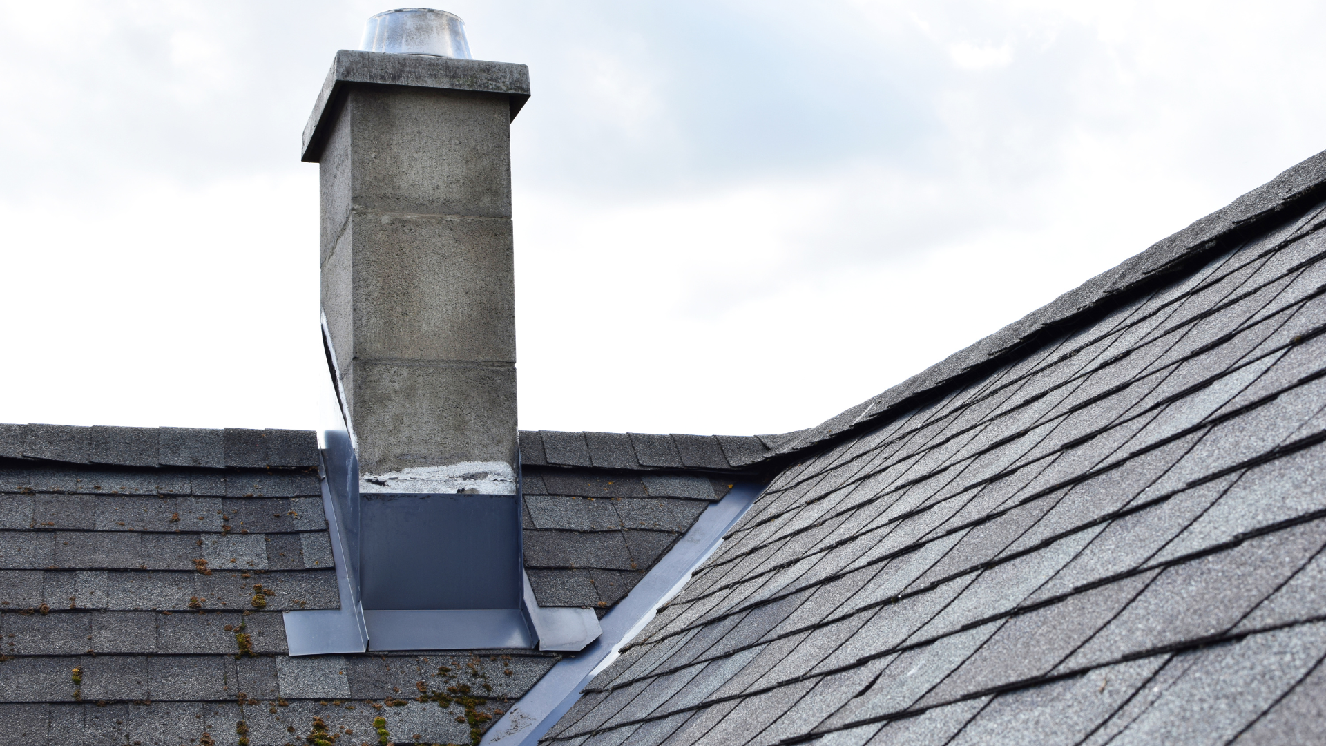 Rooftop chimney with flashing between two gray shingled roof sections