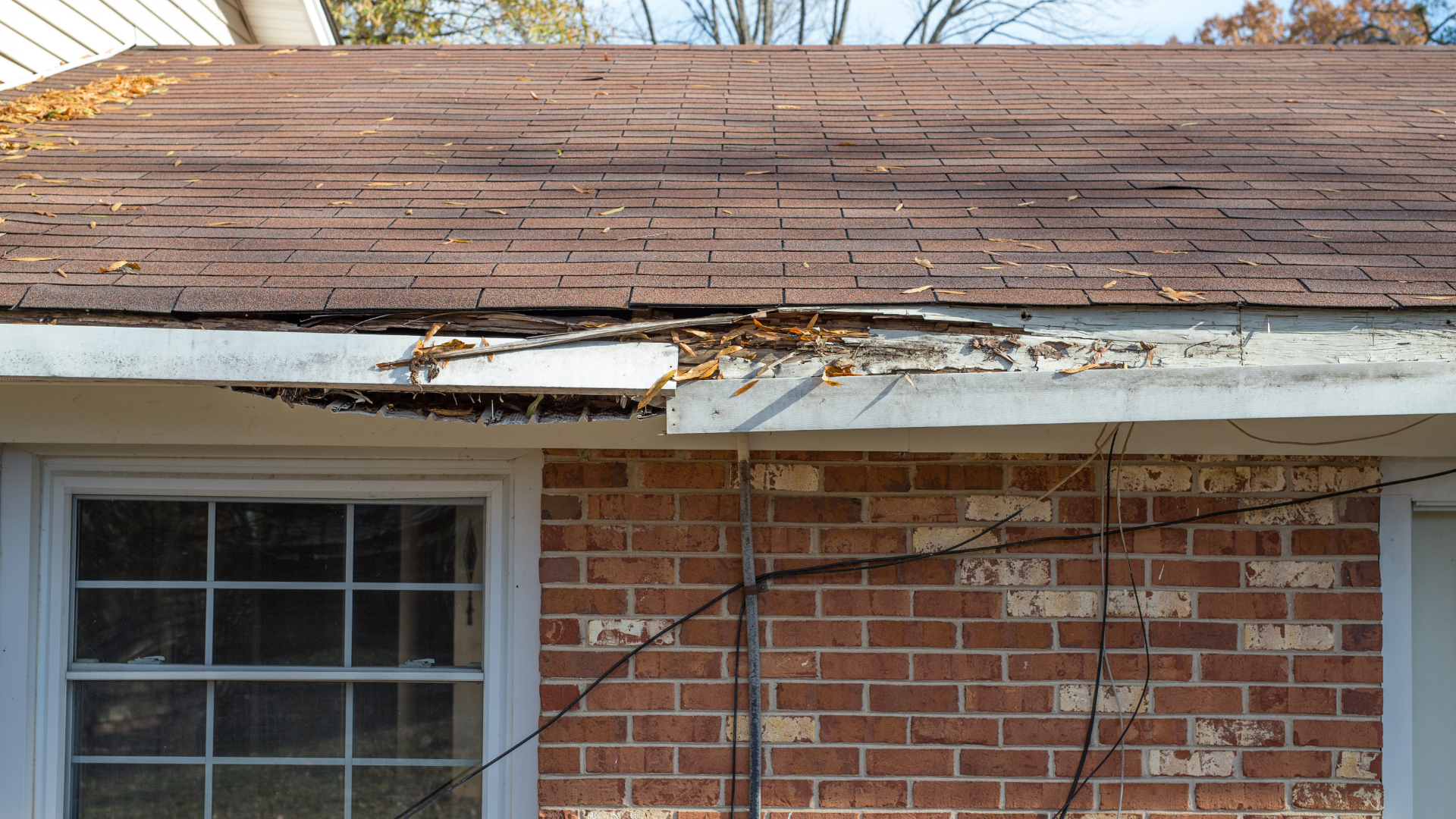 Damaged brown roof and gutter over red brick house exterior