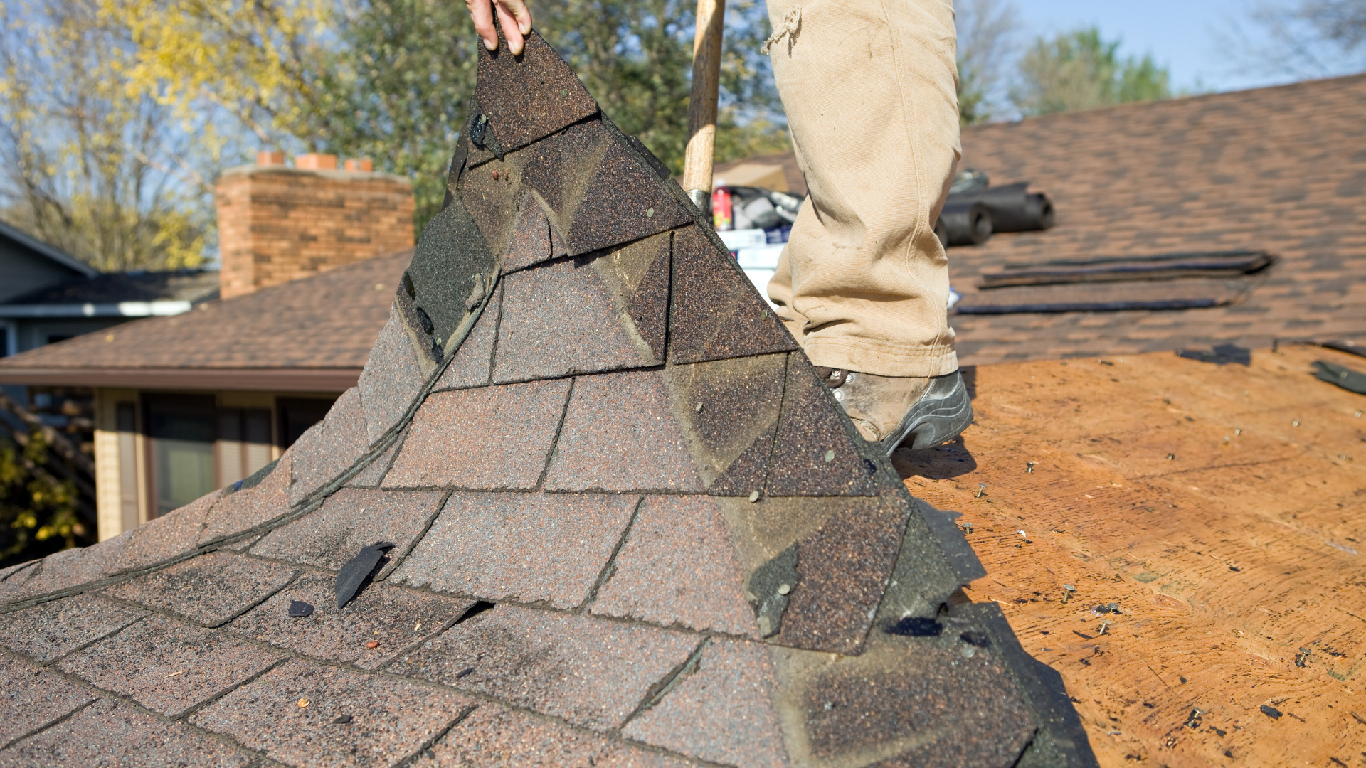 Worker lifting damaged shingles on a roof during roof repair