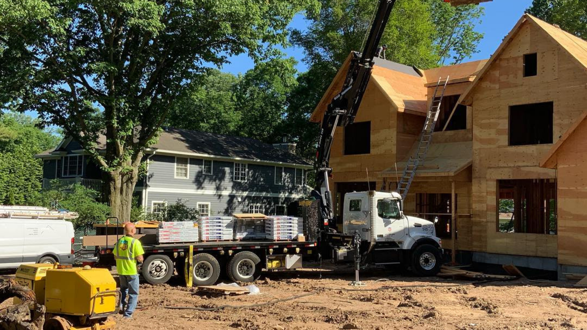 Construction site with two workers of Paese Construction LLC, a crane, and a white truck beside a house under construction