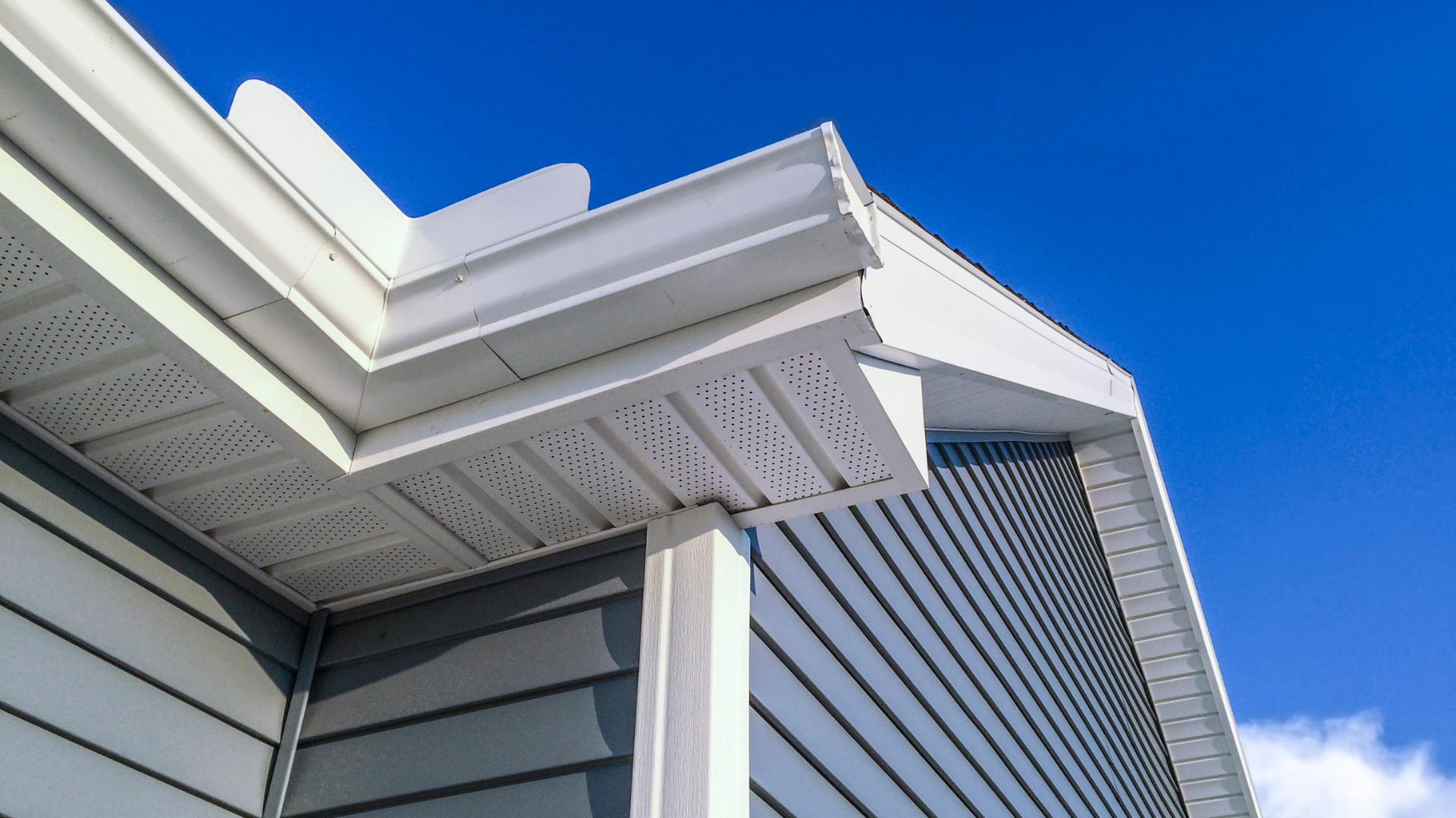 Close-up of white house eaves and gray siding against a bright blue sky