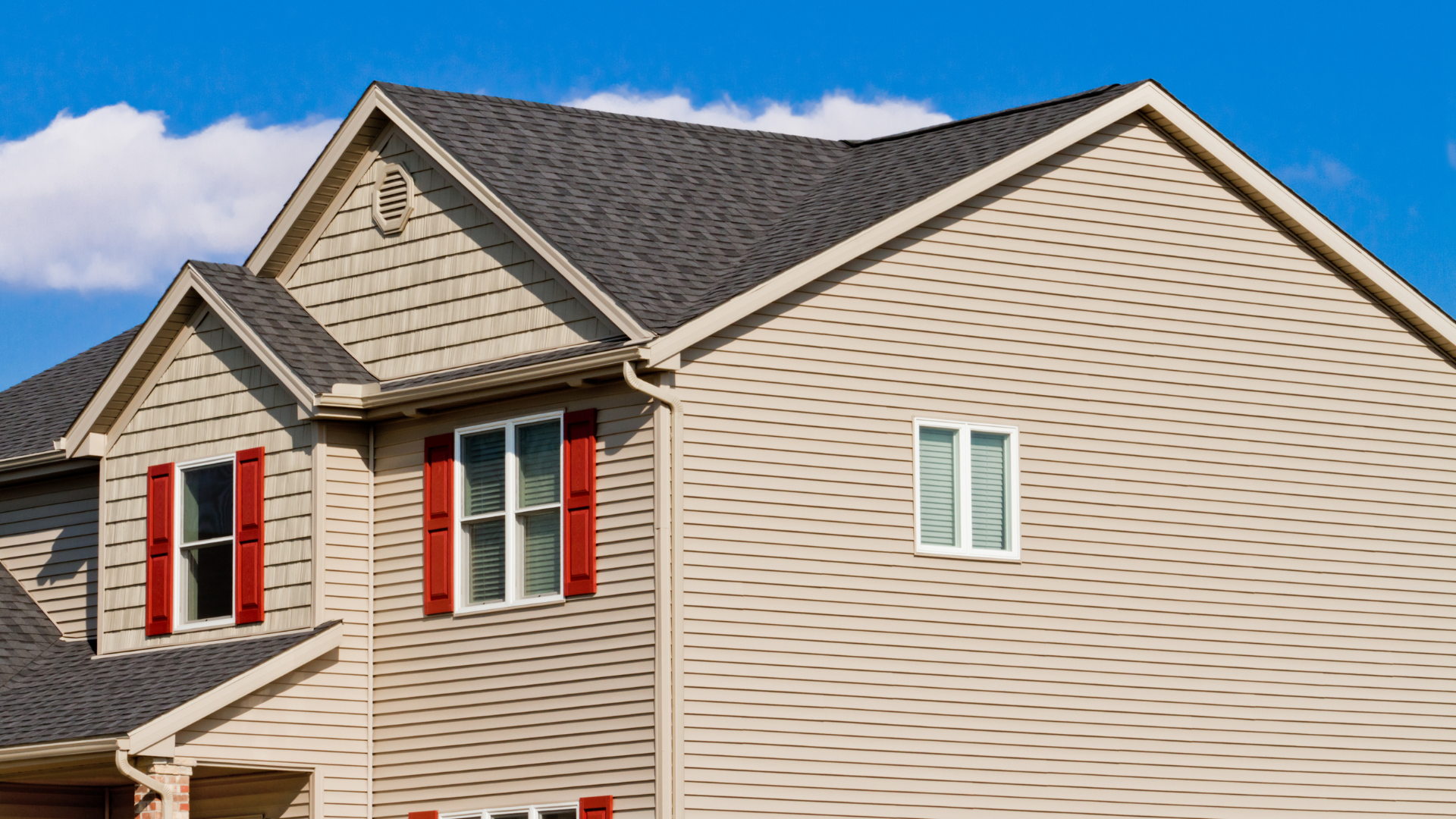 Row of beige townhouses with red shutters and gray roofs under a blue sky