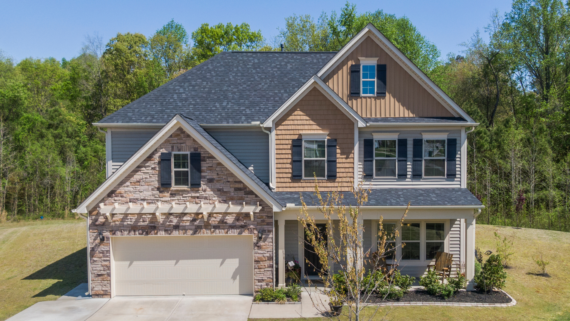 Two-story suburban house with a brick garage, gray roof, and front porch surrounded by trees