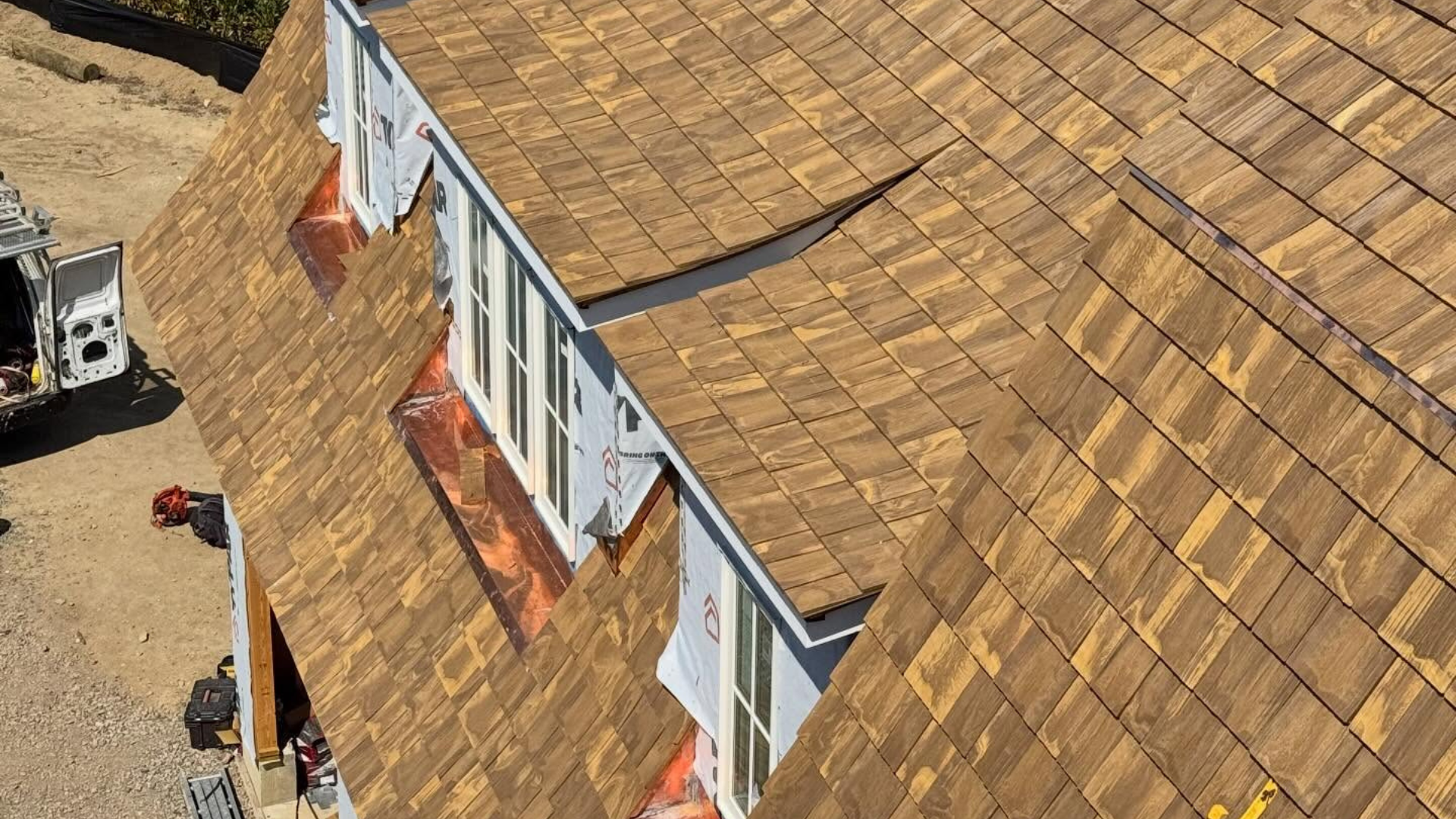 Aerial view of a tan shingled roof with dormer windows and a small chimney on the left, built by Paese Construction LLC team