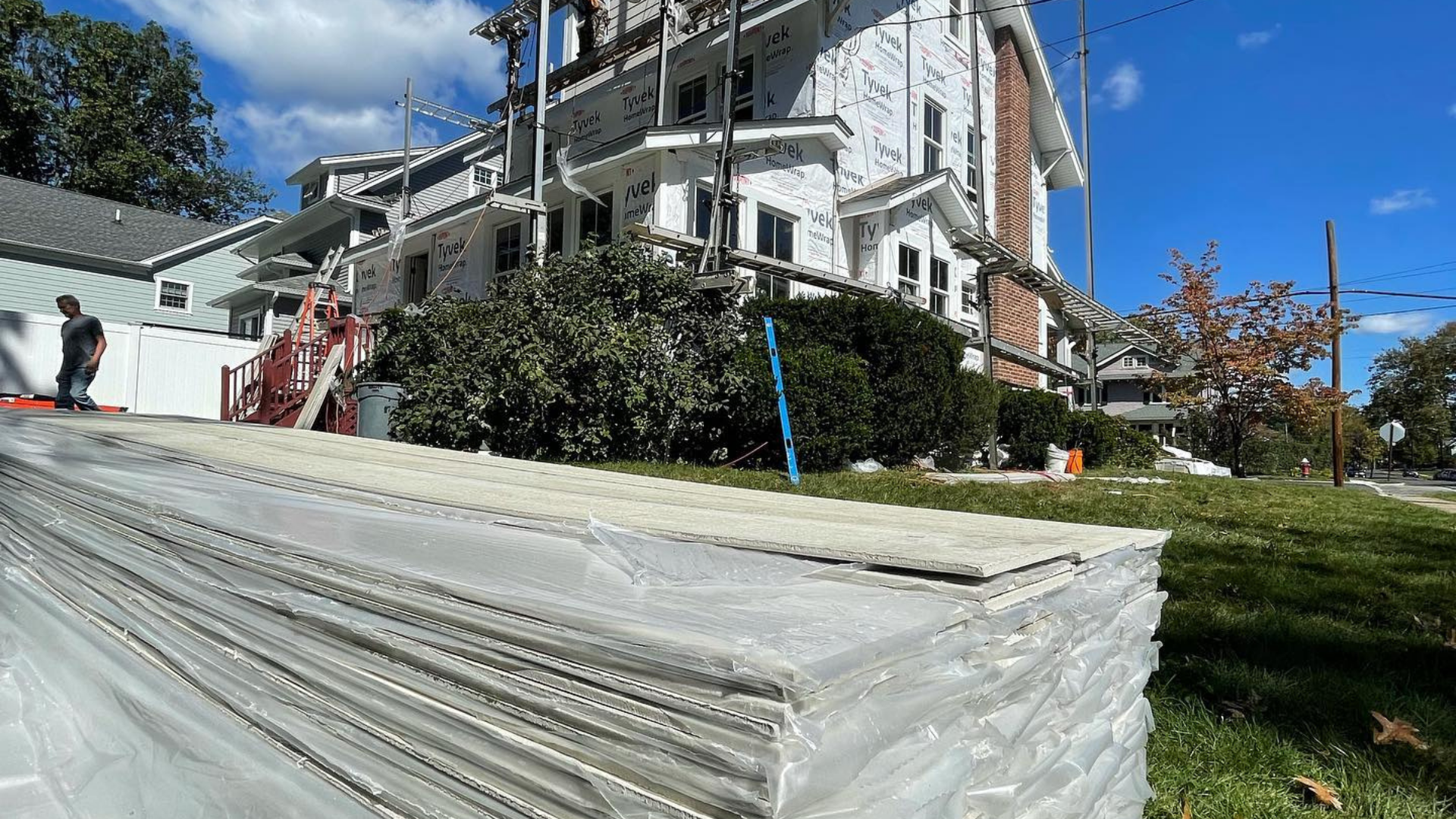 Stacked white building materials in front of a large house under a blue sky.
