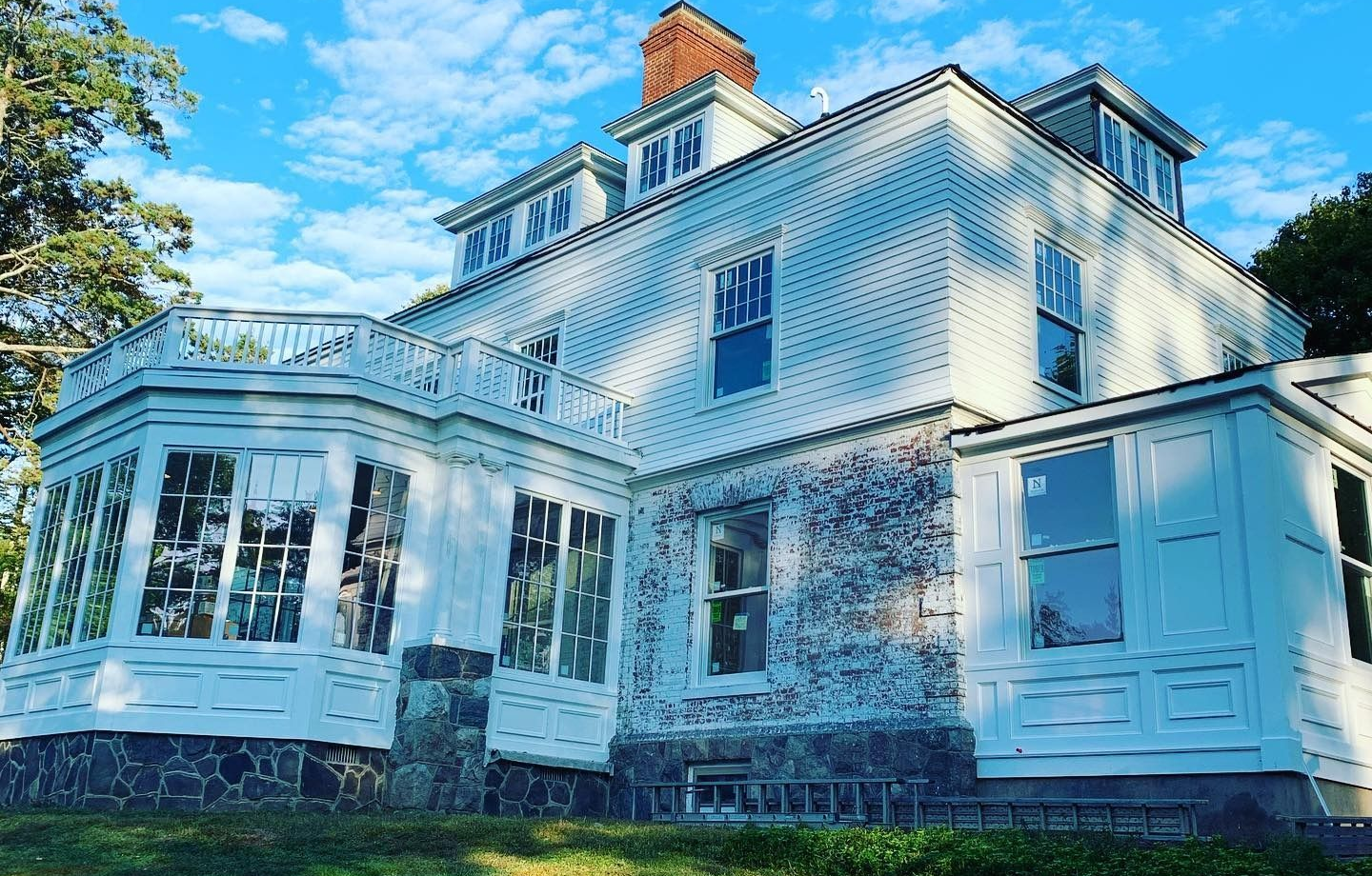 White multi-story house with sunroom, under a blue sky.