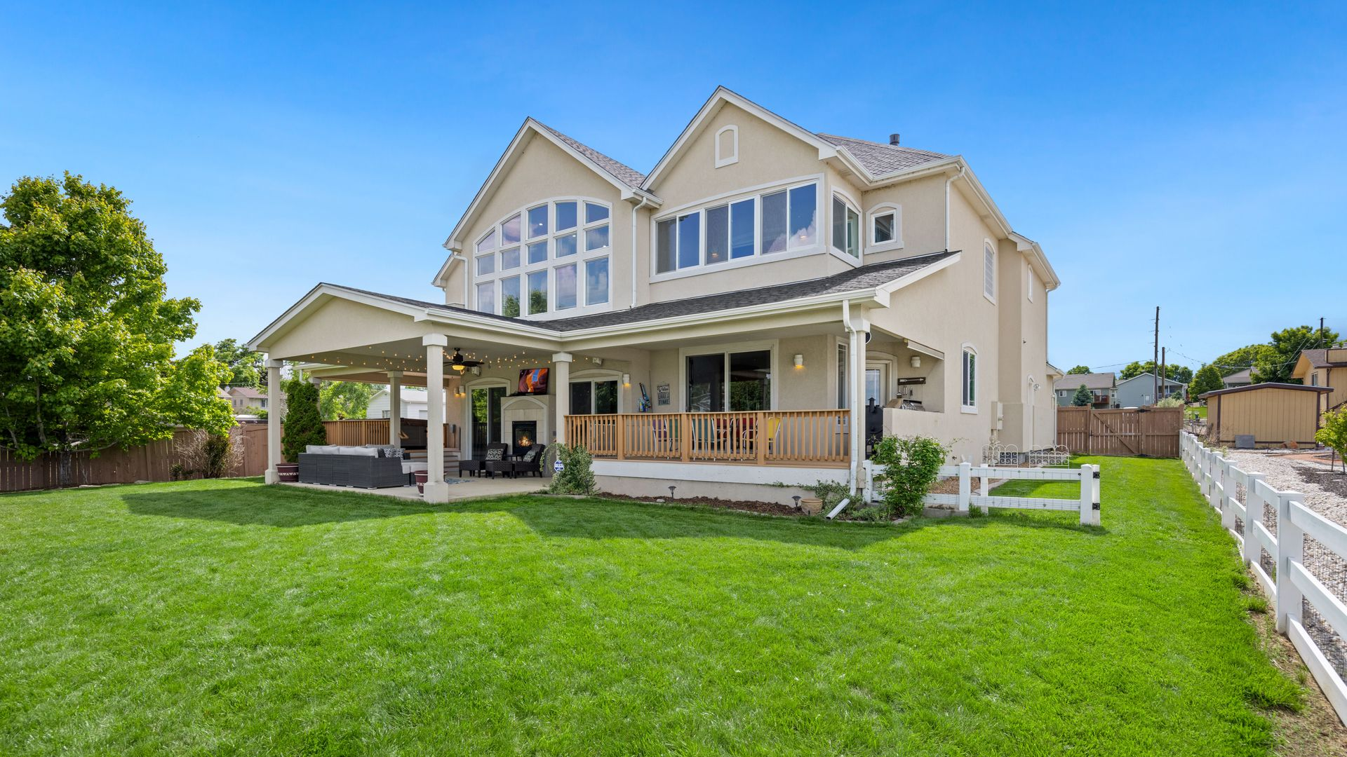 Large beige two-story house with a covered patio and a bright green lawn