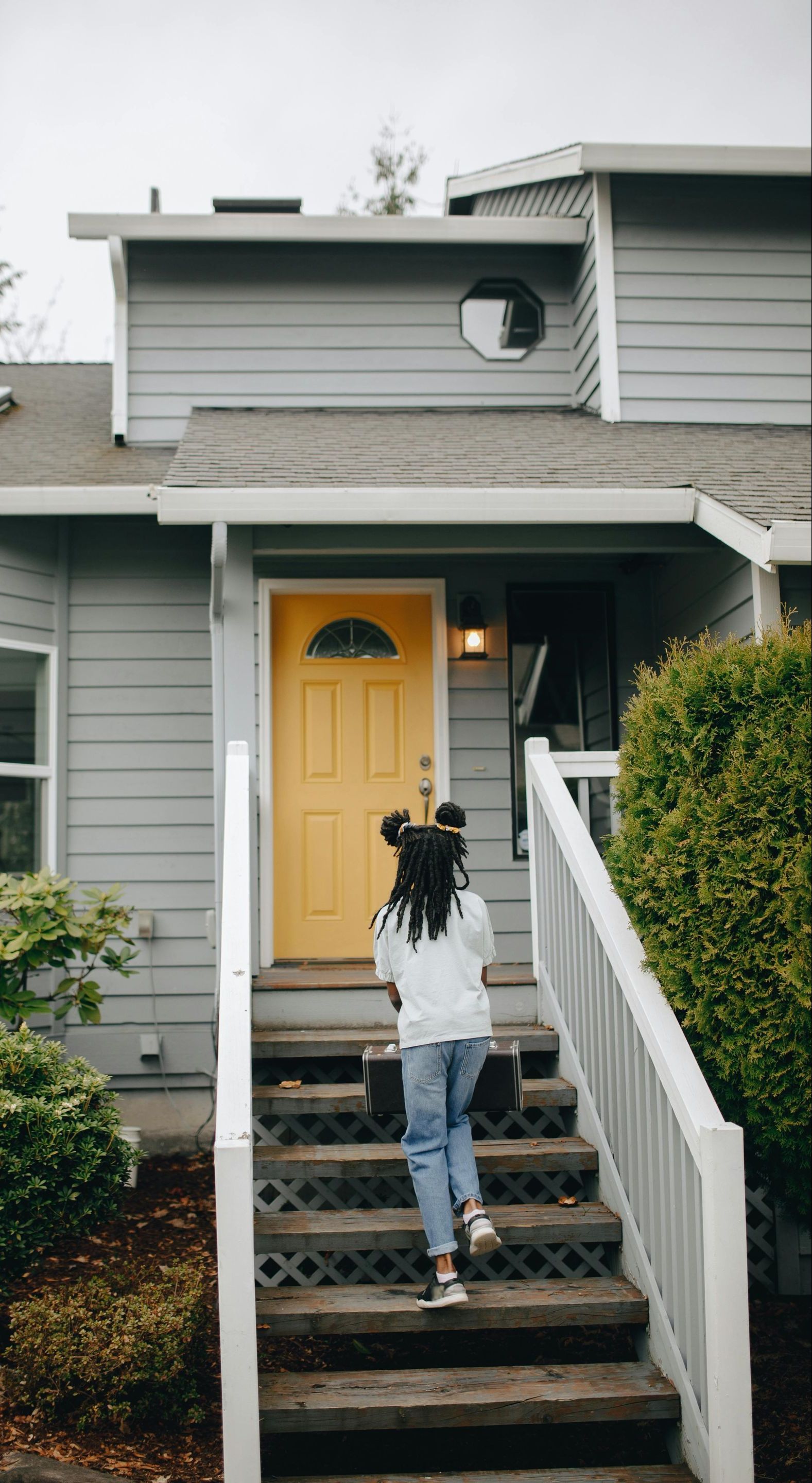A woman is walking up the stairs to a house with a yellow door.