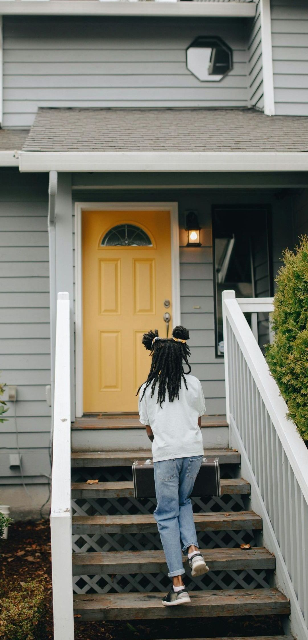 A woman is walking up the stairs to a house with a yellow door.