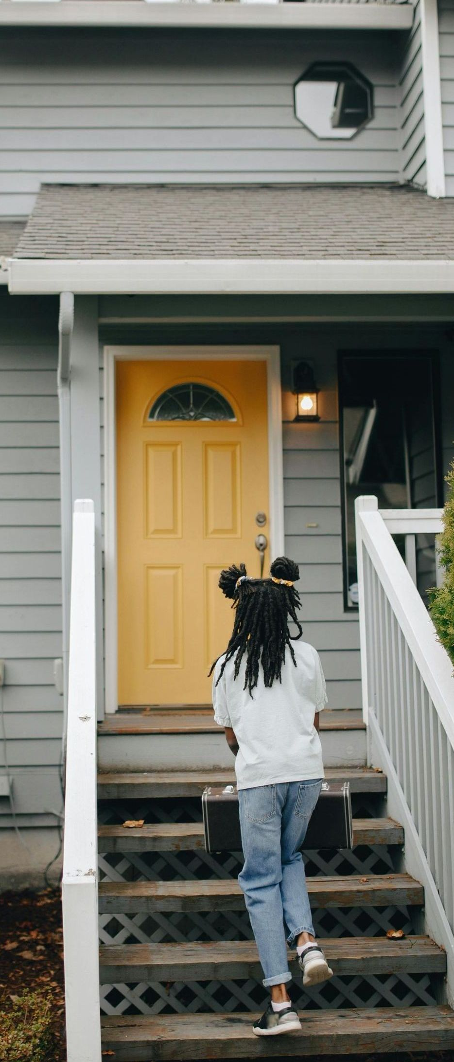 A woman is walking up the stairs to a house with a yellow door.