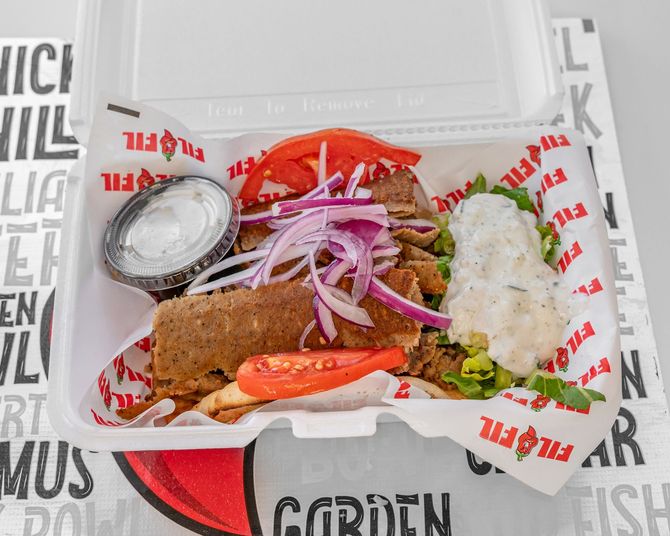 Gyro meal in a takeout container with meat, vegetables, and tzatziki sauce.