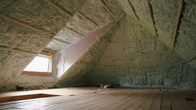 Attic with wooden floor and walls covered in green insulation, including around a window.