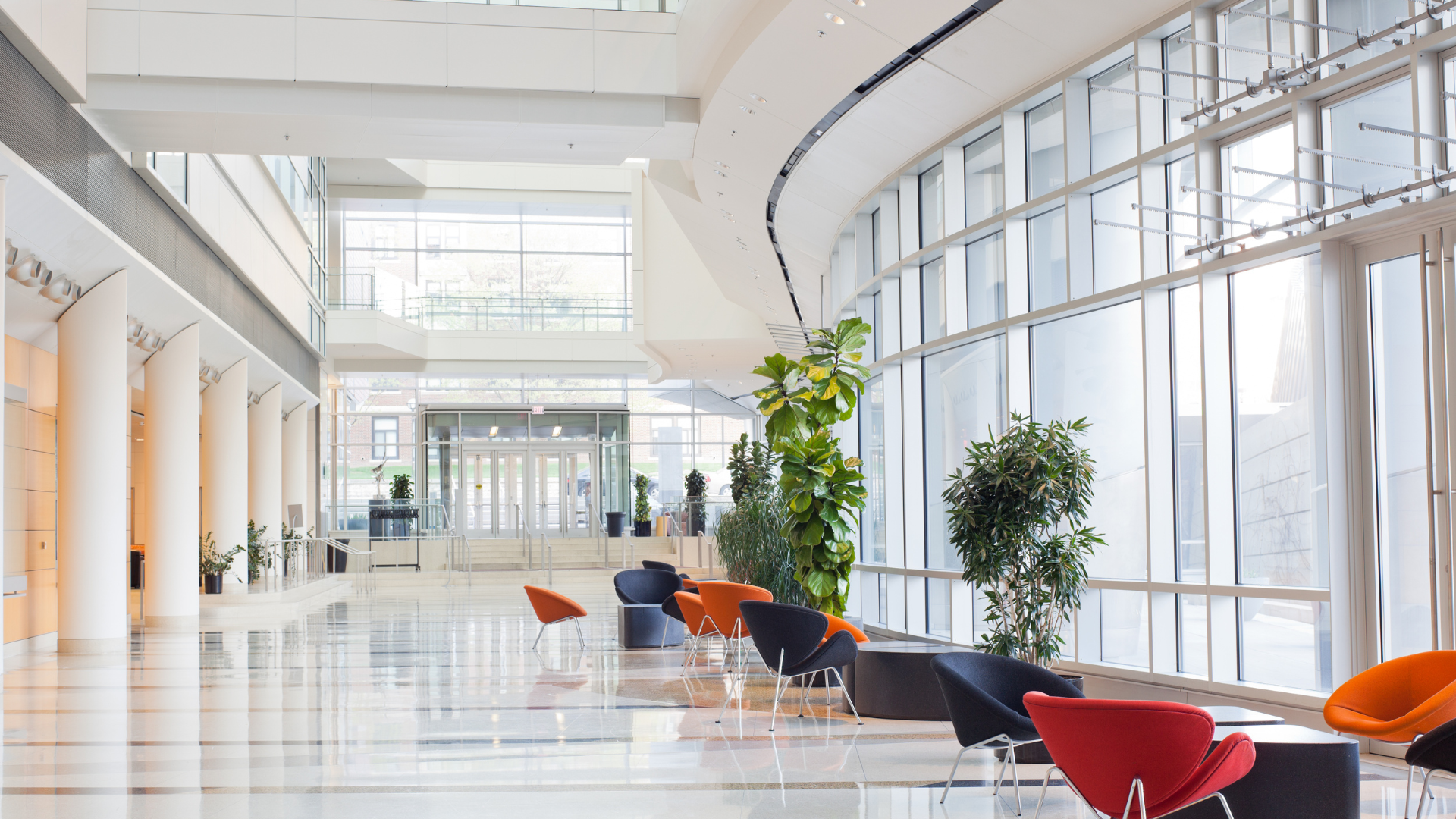 Spacious, modern lobby with marble floors, columns, curved glass wall, and colorful seating.