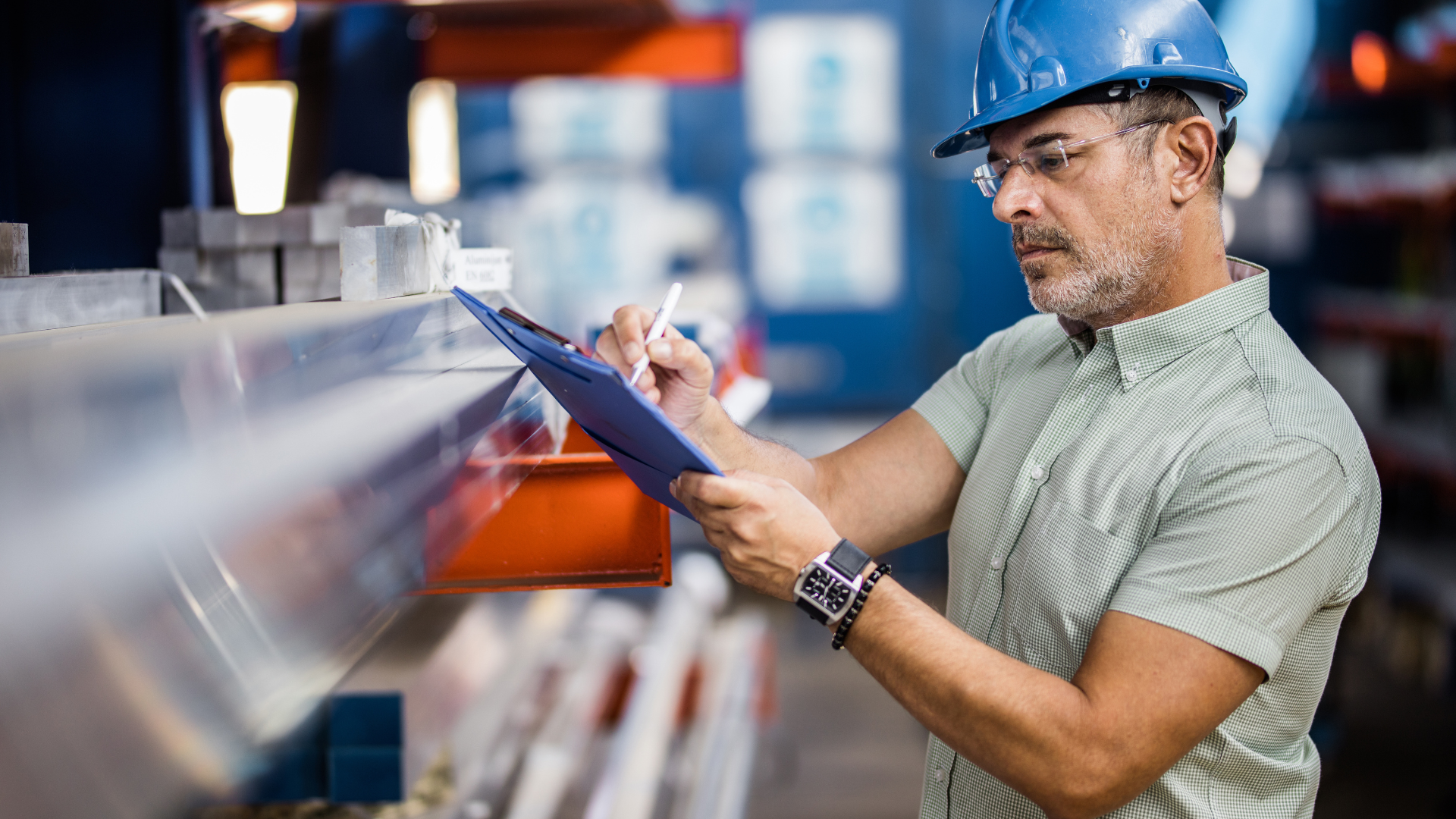 Worker in blue hard hat inspecting warehouse shelves with a clipboard