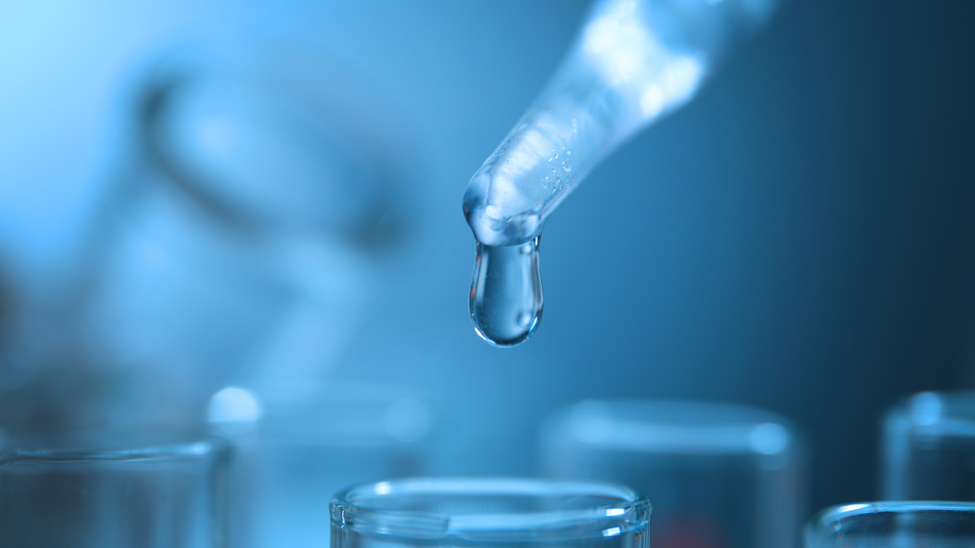 Droplet falling from a pipette into a test tube; blue-toned lab setting.