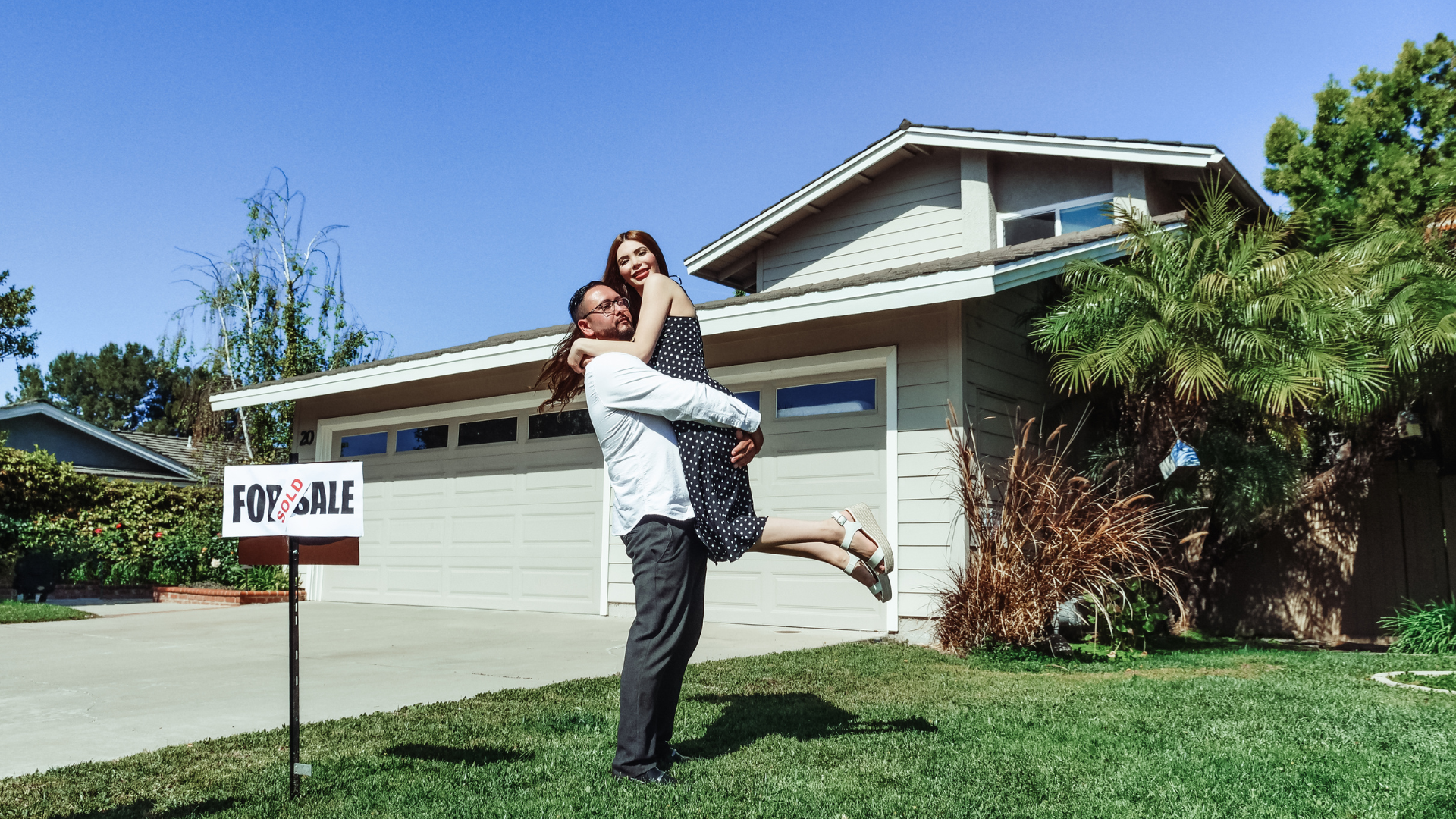 A person holding another person in their arms in front of a suburban house with a