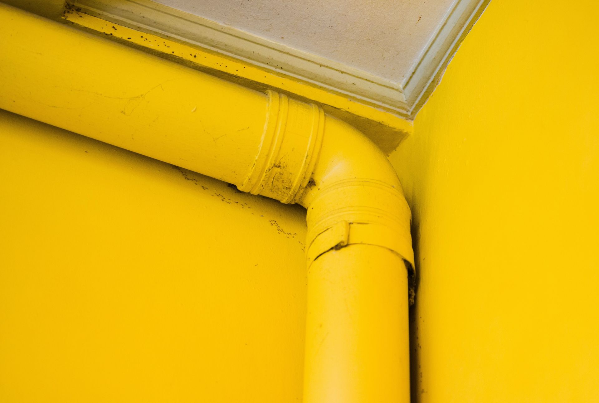 Yellow wall-mounted pipe with a 90-degree bend near the ceiling corner