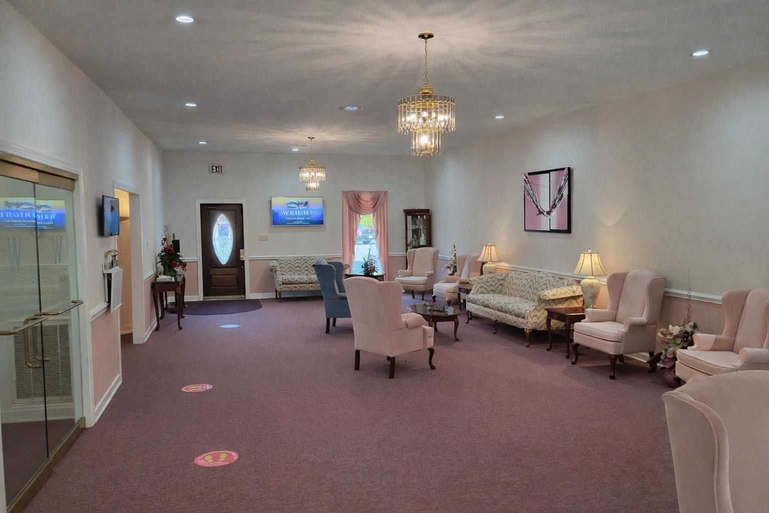 Spacious waiting room with beige chairs, purple carpet, chandelier, wall art, and a front door with windows