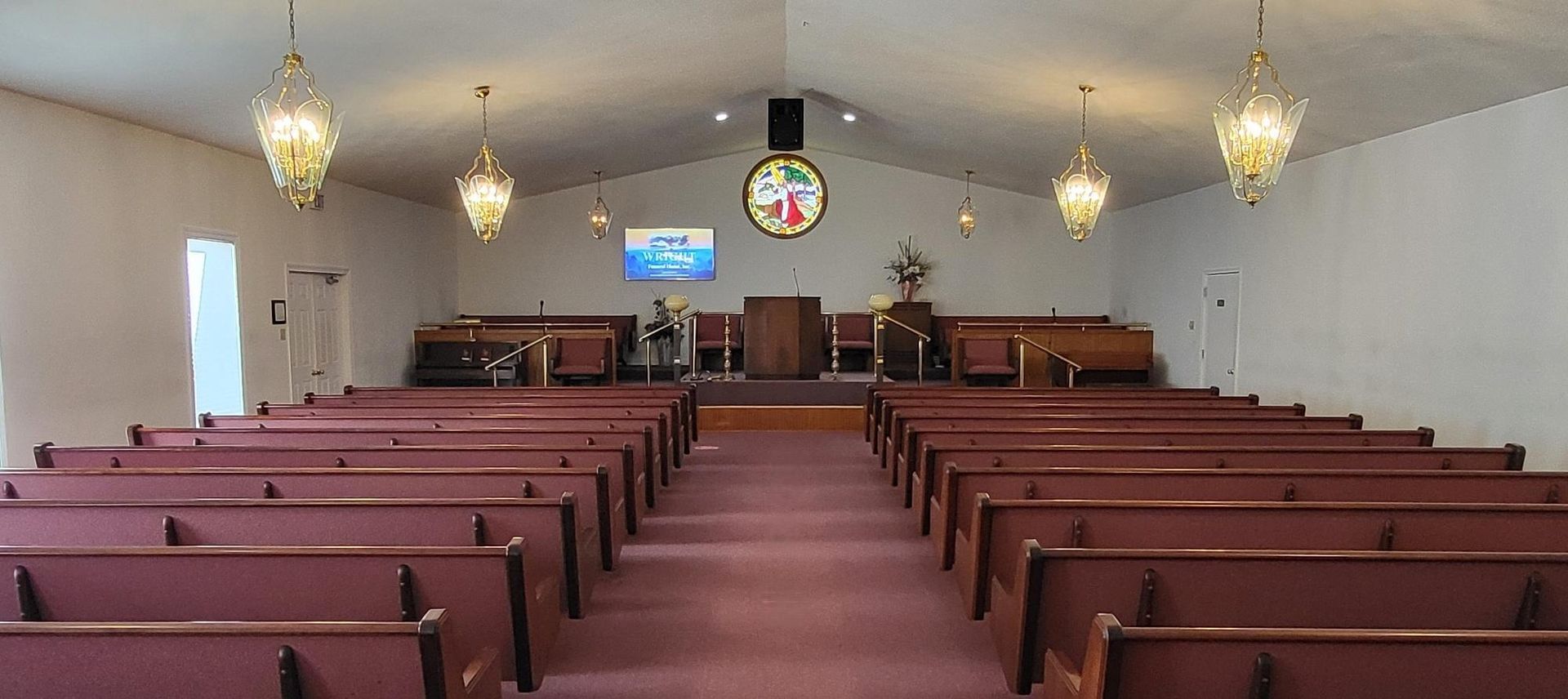 Empty church interior with rows of pews, chandeliers, and a pulpit at the front