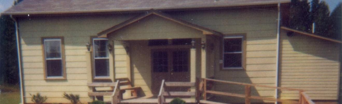 Front view of a beige house with a small porch, wooden railing, and front steps