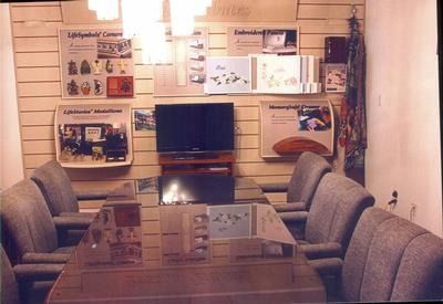 Display room with sofas, glass coffee table, and wall-mounted information panels around a TV.