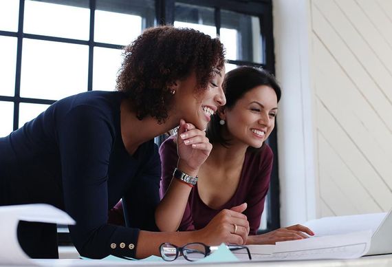 Two women are looking at a laptop together and smiling