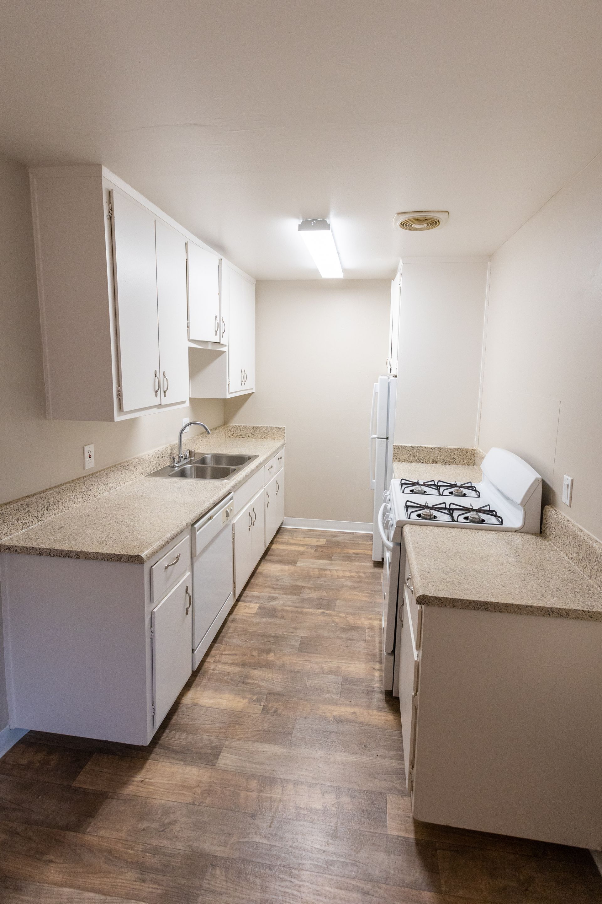 Narrow kitchen with white cabinets, speckled countertops, wood-look floor, and stove by the back wall