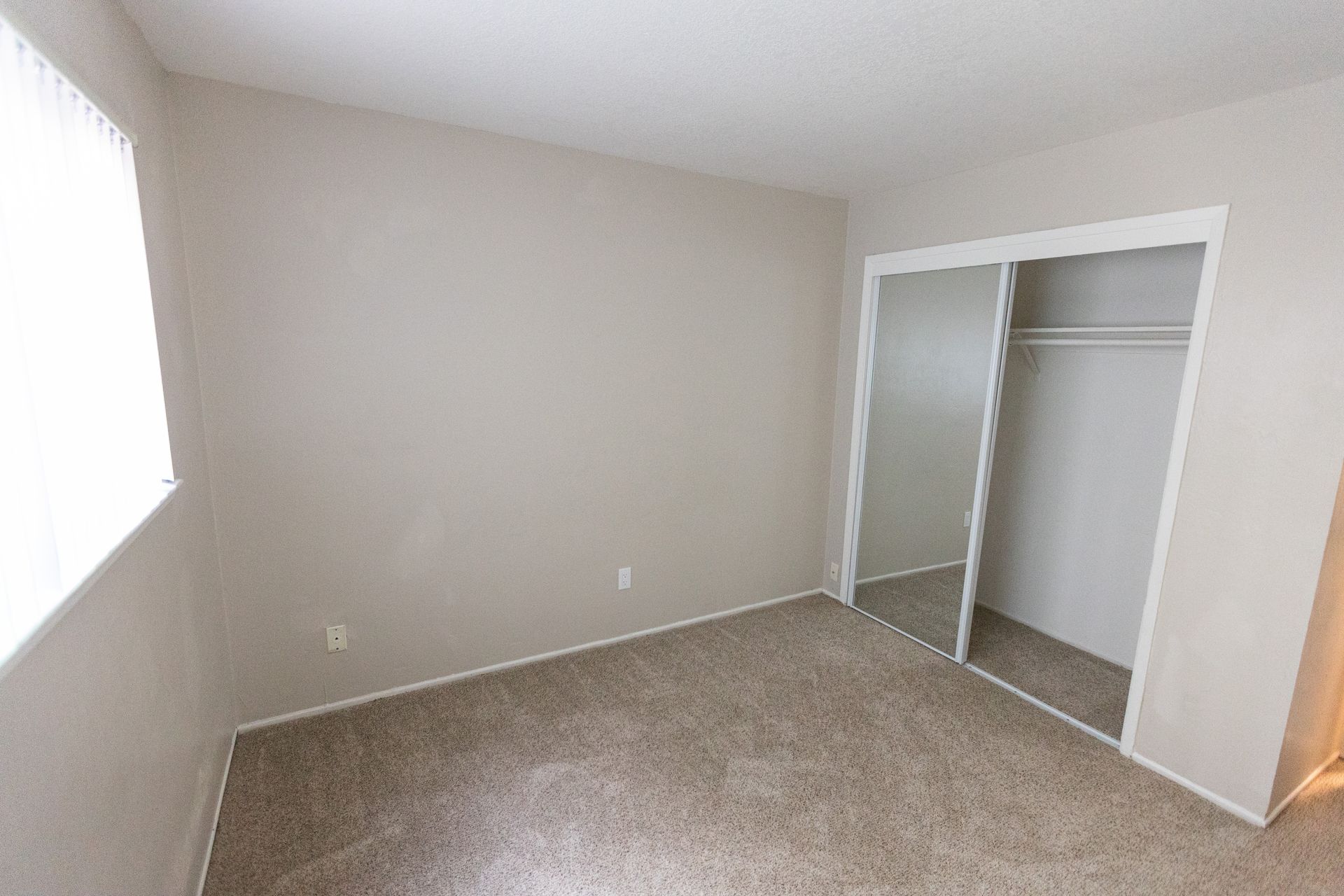 Empty beige bedroom with carpet, window light, and an open closet.