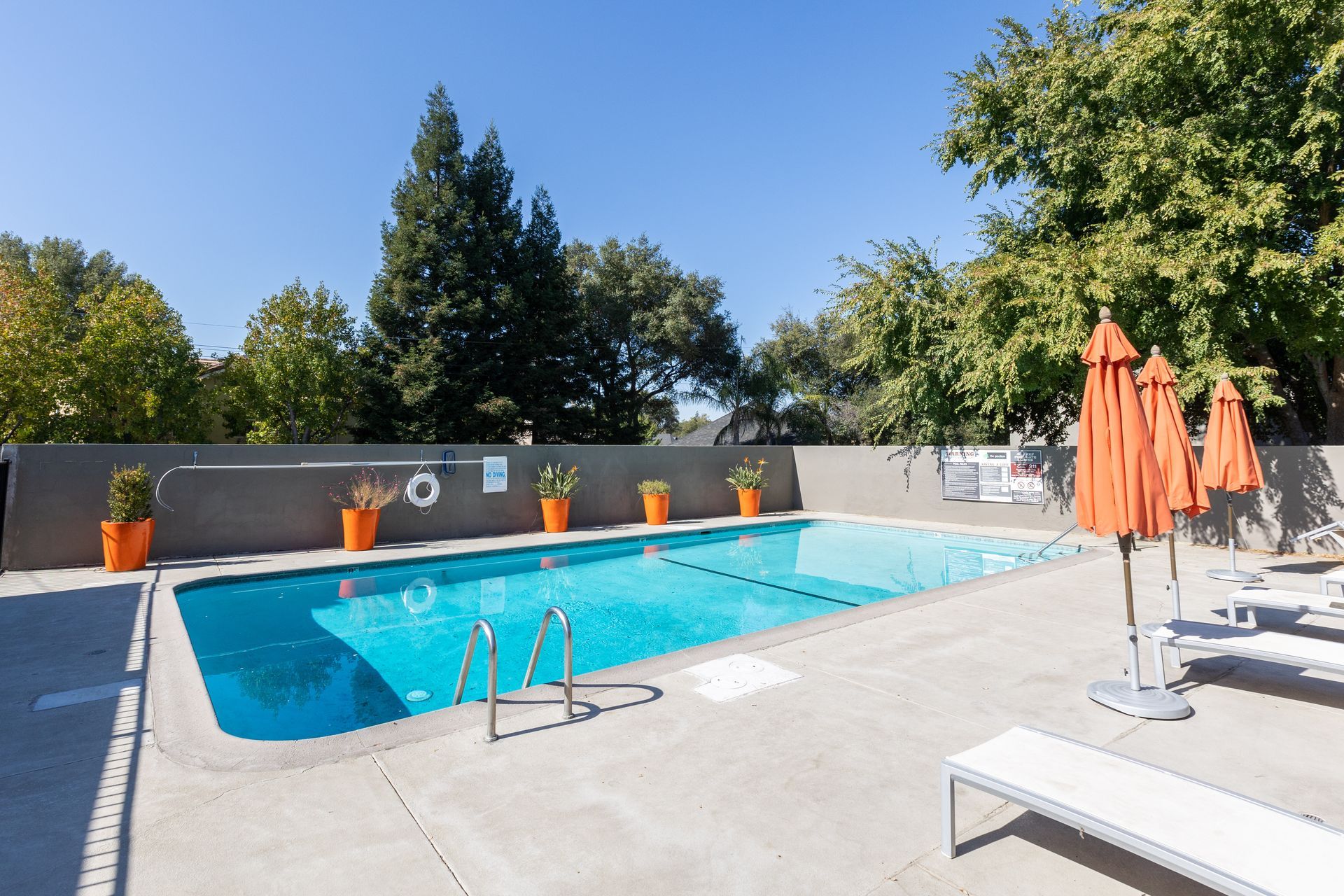Outdoor pool with blue water, orange umbrellas, and lounge chairs on a sunny patio