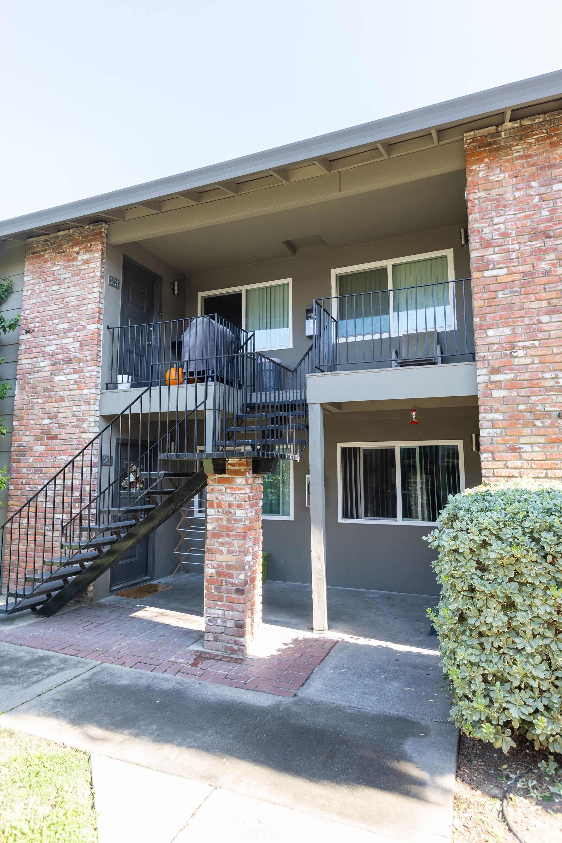 Apartment building exterior with brick facade, staircase, and second-floor balconies under an overhang