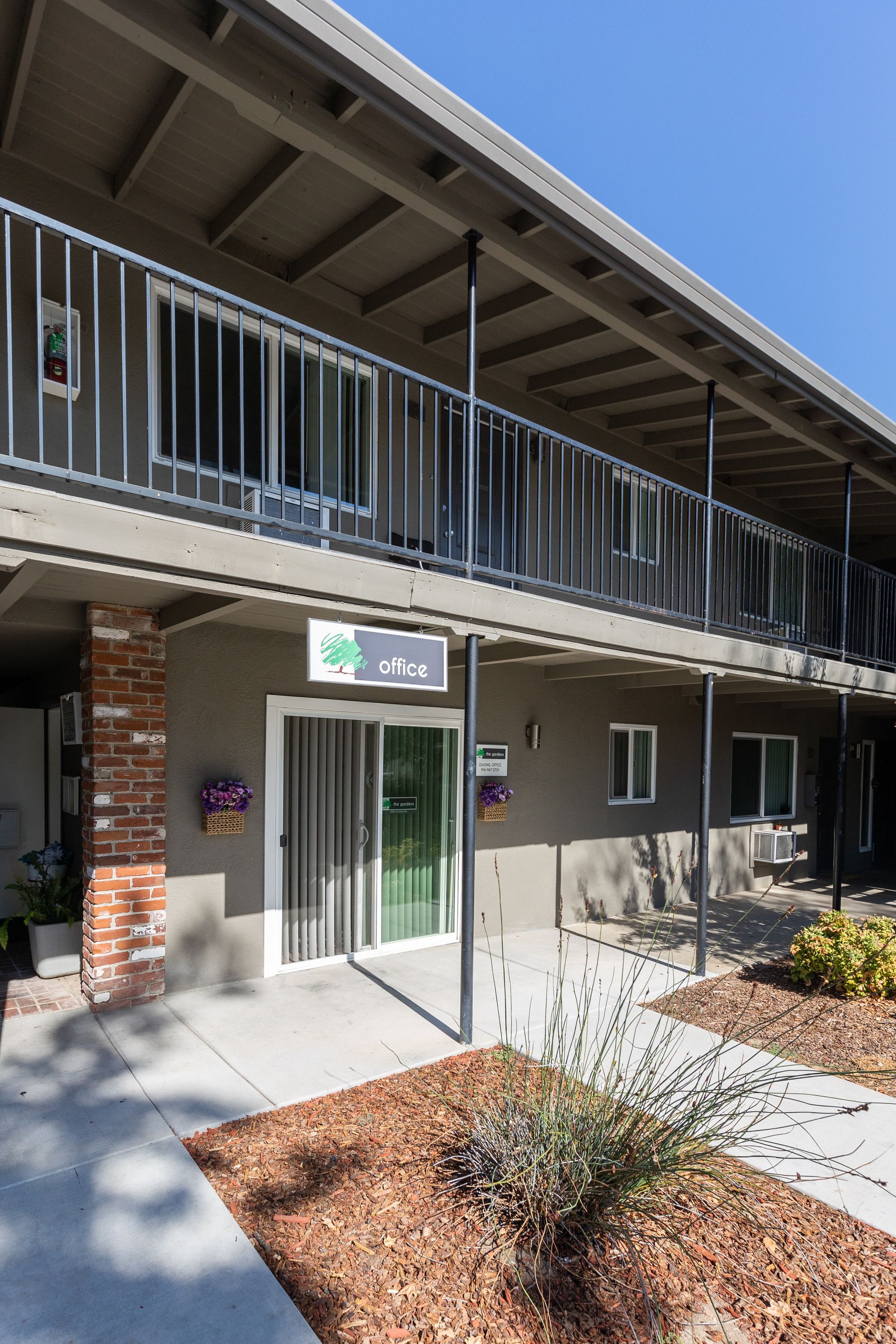 Exterior of a two-story apartment building with balconies, brick walls, and a glass entrance door