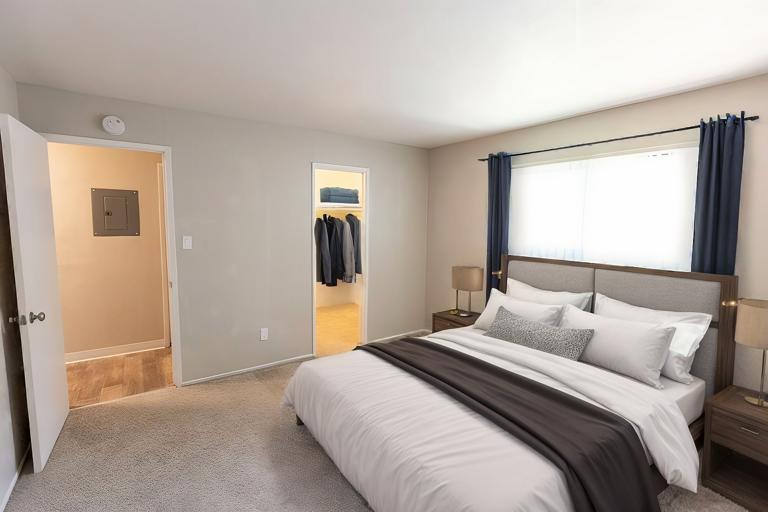 Bright bedroom with a made bed, gray carpet, and open doors leading to a closet and bathroom.