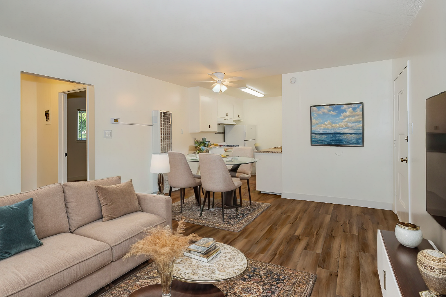 Bright living room with beige sofa, dining area, wood floors, and coastal wall art