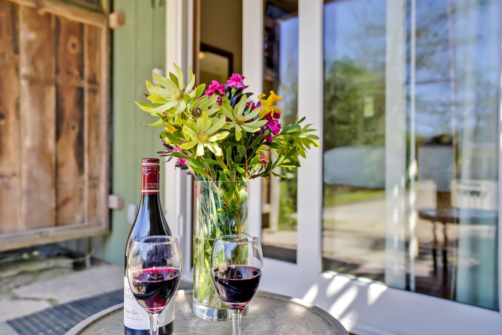 A bottle of wine and two glasses of wine are on a table next to a vase of flowers.