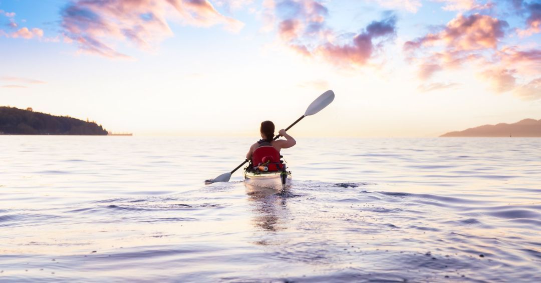 woman kayaking in the ocean with a blue sky and pink clouds