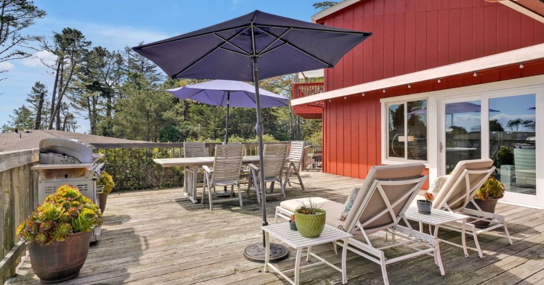 outdoor deck with table and chairs, grill, blue shade umbrellas, and chaise lounges at bodega bay inn