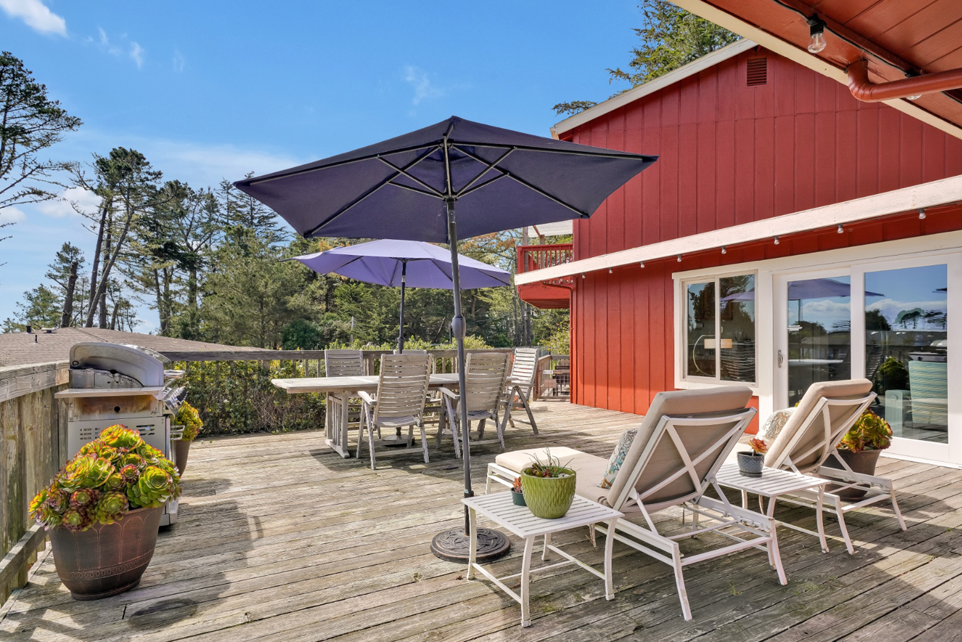 A deck with chairs and umbrellas in front of a red house