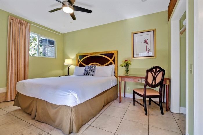 A hotel room with a king size bed , desk , chair and ceiling fan.