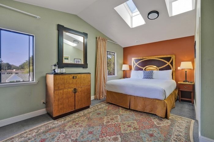 A bedroom with a king size bed , dresser , nightstand , mirror and skylight.
