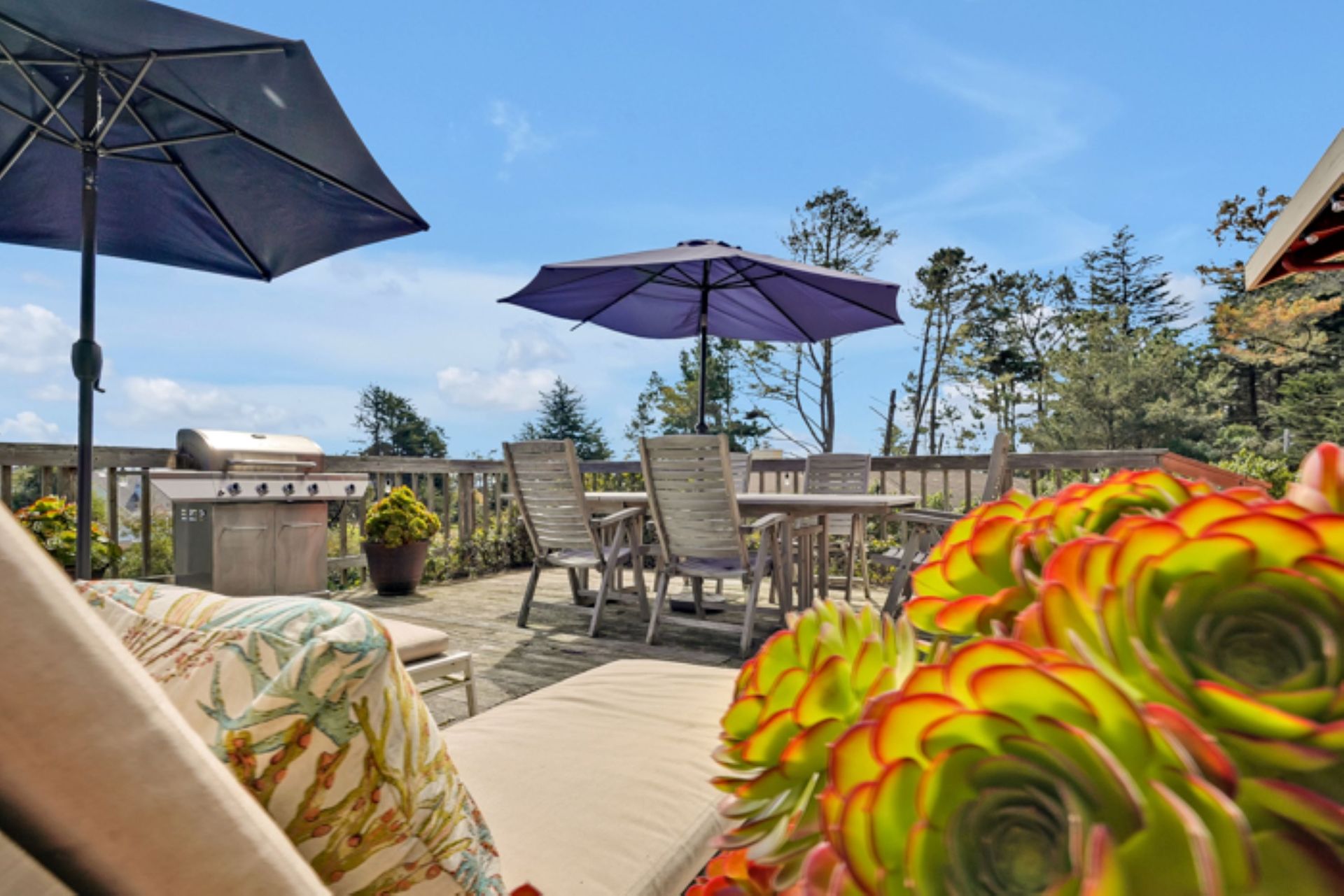 A patio with umbrellas , chairs , a table and a grill.