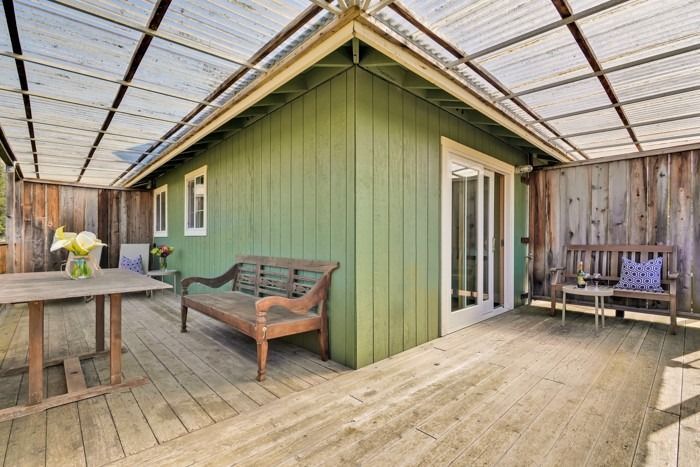 A green house with a wooden deck and a bench.