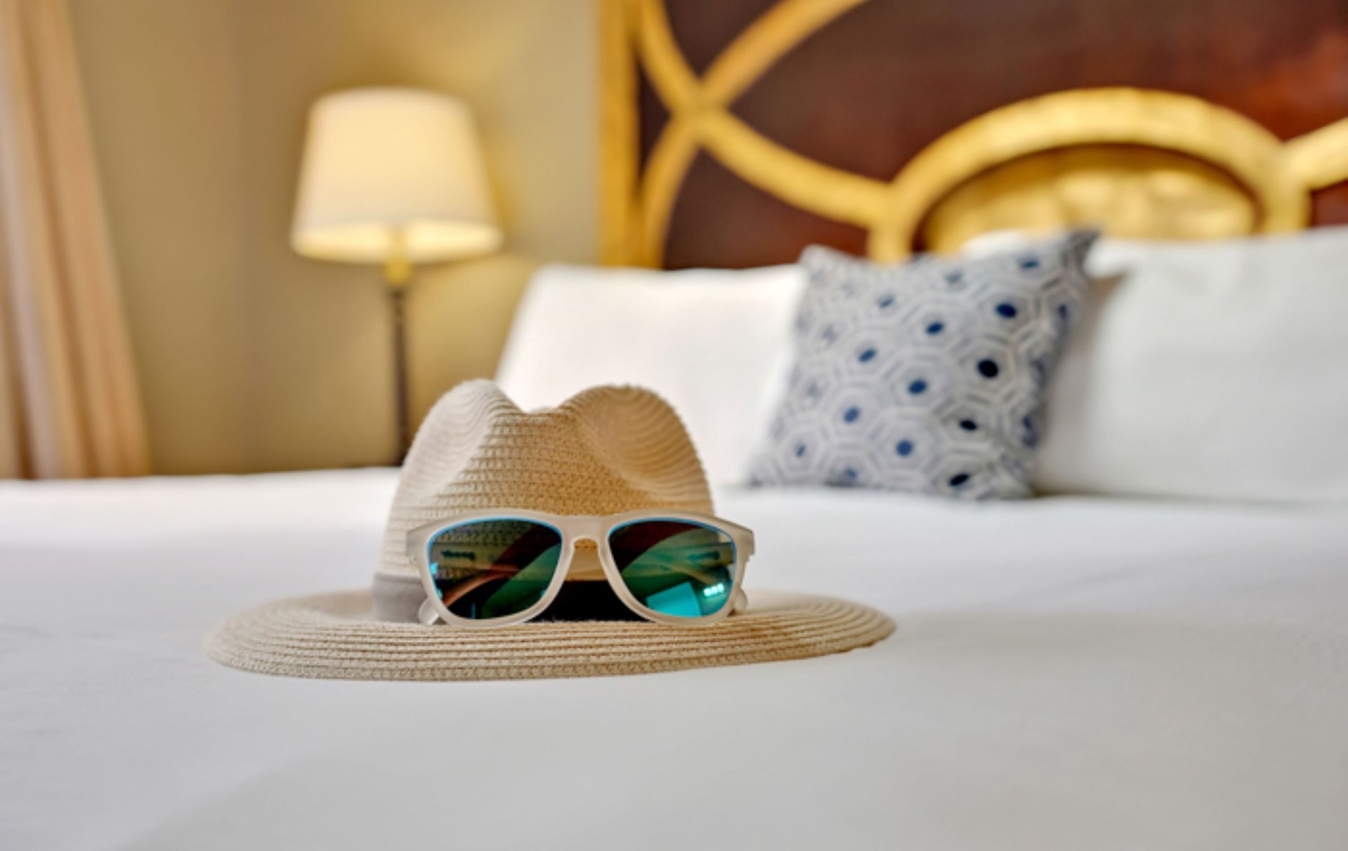 A hat and sunglasses are on a bed in a hotel room