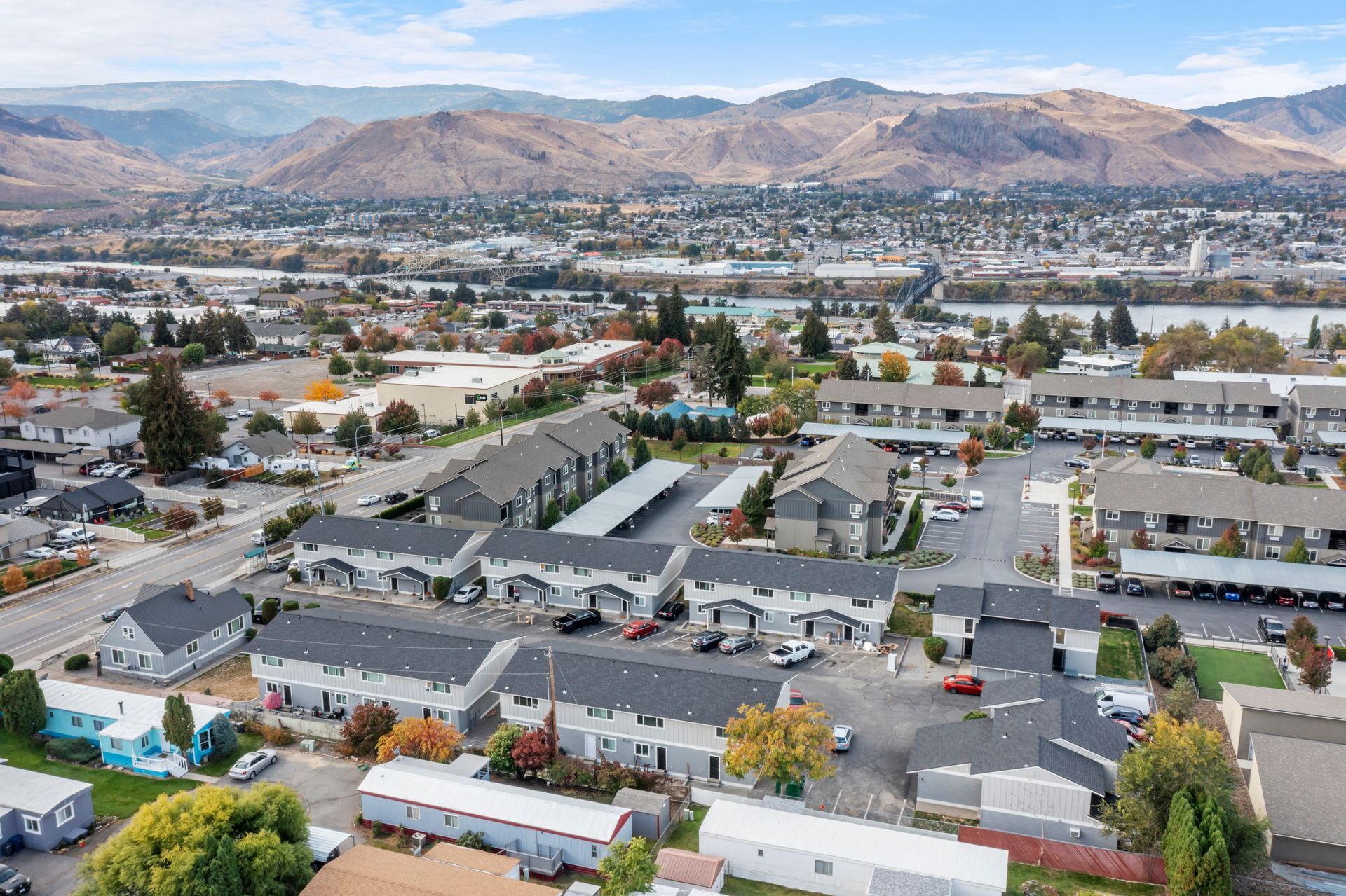 Aerial view of townhouses in a valley with mountains and a river in the background.