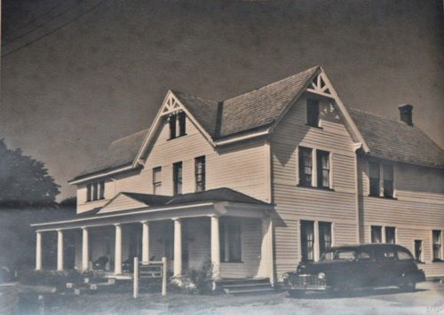 A black and white photo of a house with cars parked in front of it