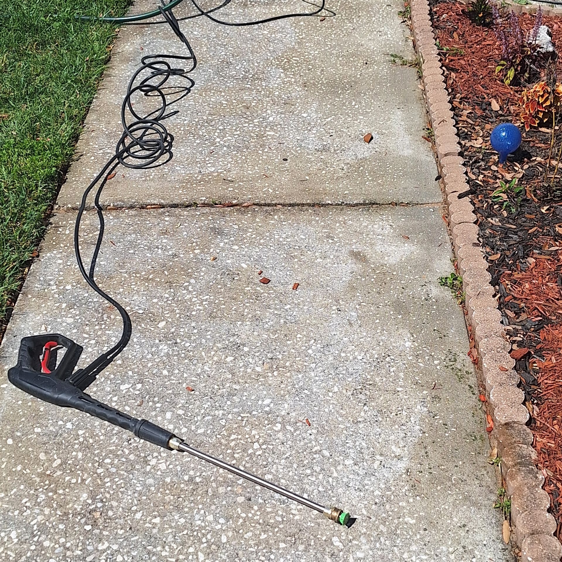 A high pressure washer is sitting on a sidewalk next to a garden.