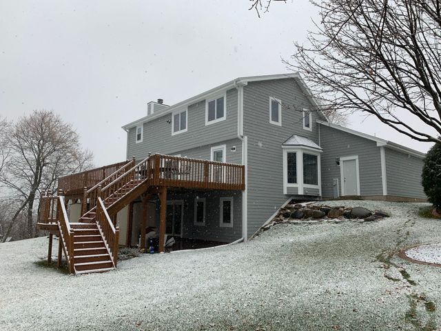 Gray house with wooden deck on a snowy hillside, bare trees in the background